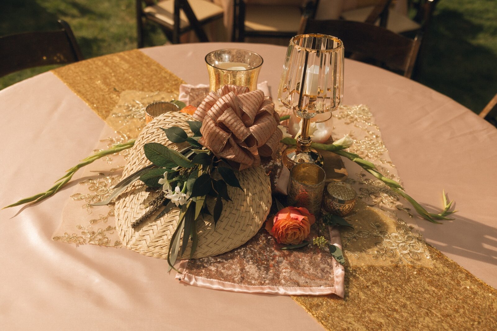 Detailed centerpiece on a blush tablecloth featuring a woven fan, blush bow, and an orange garden rose.