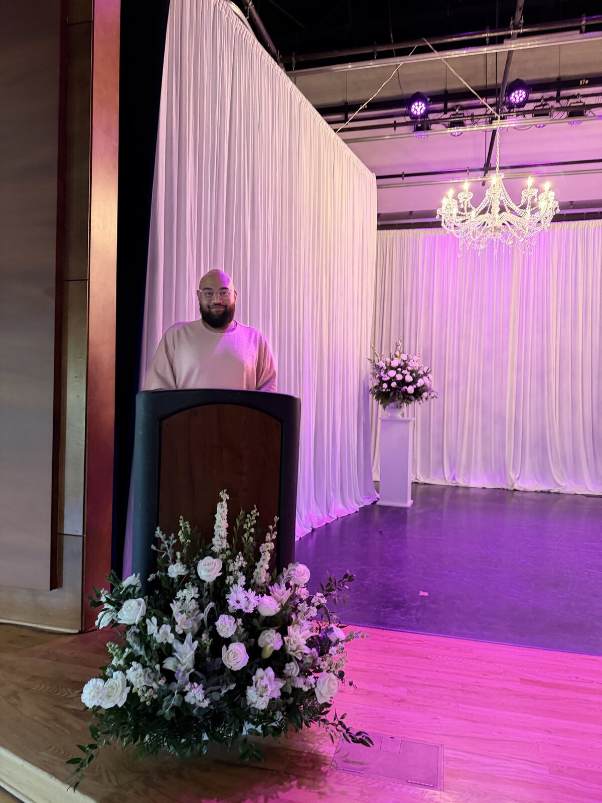 Podium floral arrangement and white draped backdrop for the Miss West Valley City event.